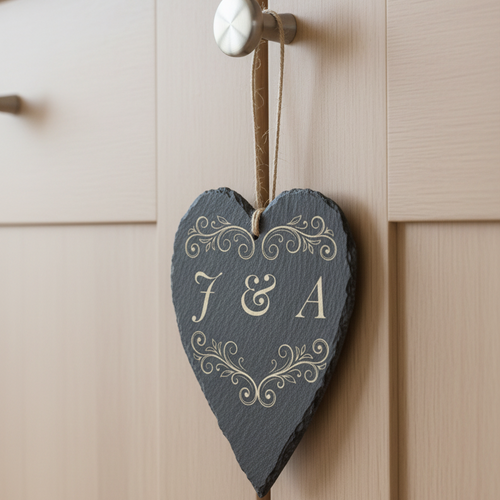 A heart-shaped dark slate hanging ornament with decorative scroll work and the initials 'J & A', suspended by a twine loop from a door knob on a light wood cabinet.