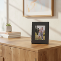 A rectangle black picture frame with an inset photograph of a family outdoors.