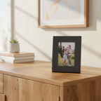 A rectangle black picture frame with an inset photograph of a family outdoors.