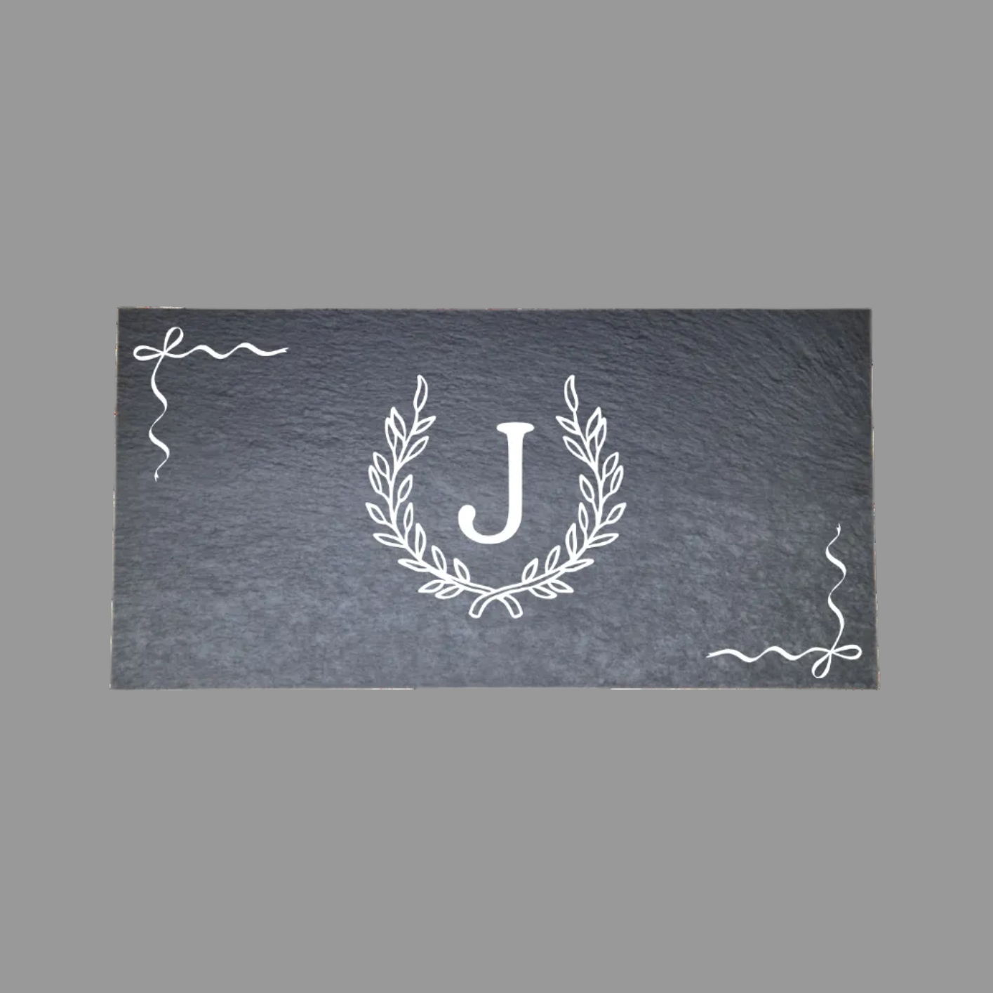 A rectangular dark gray slate sign with a white engraved monogram 'J' inside a laurel wreath, accented with scroll designs in the corners.