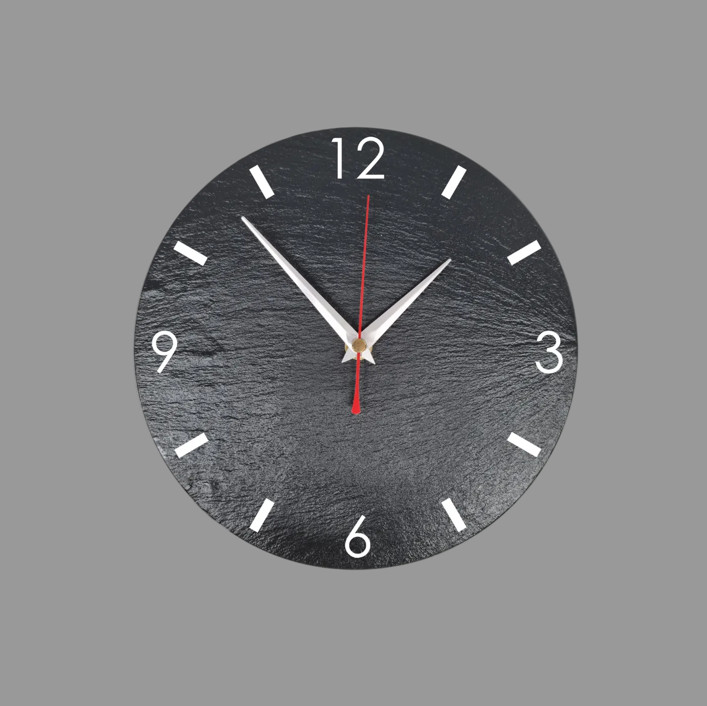 A minimalist round wall clock with a dark textured slate face, numerals, and silver hands with a red second hand, shown against a solid gray background.